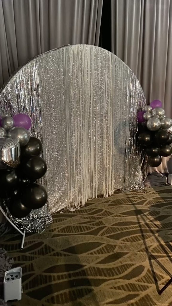 Silver sequin arched backdrop with black, silver, and purple balloon clusters
