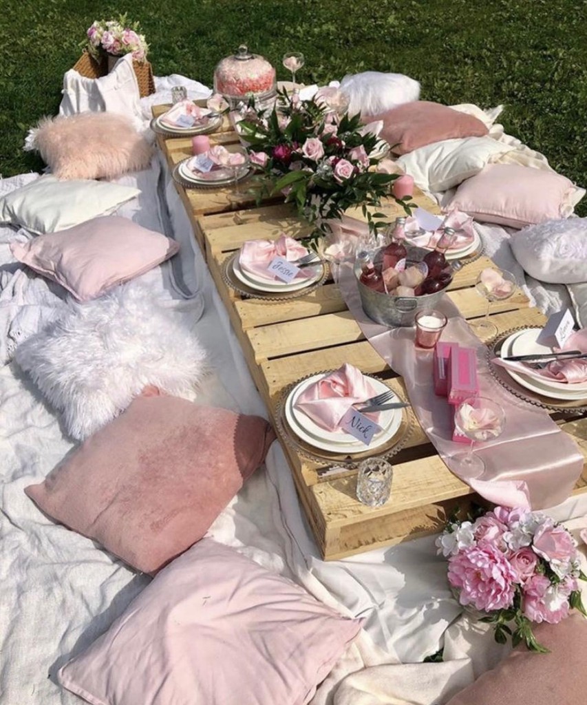 Luxury outdoor picnic with a wooden pallet table, pink pillows, and florals