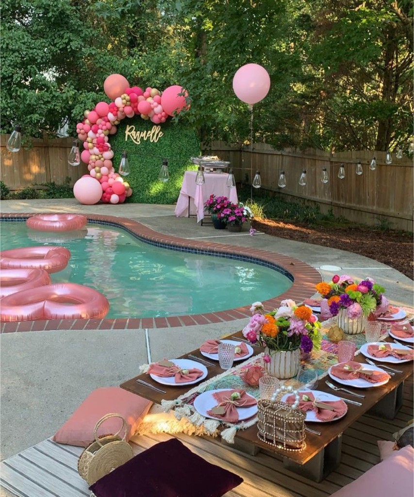 Poolside pink picnic with balloon arch, heart floats, and low dining table